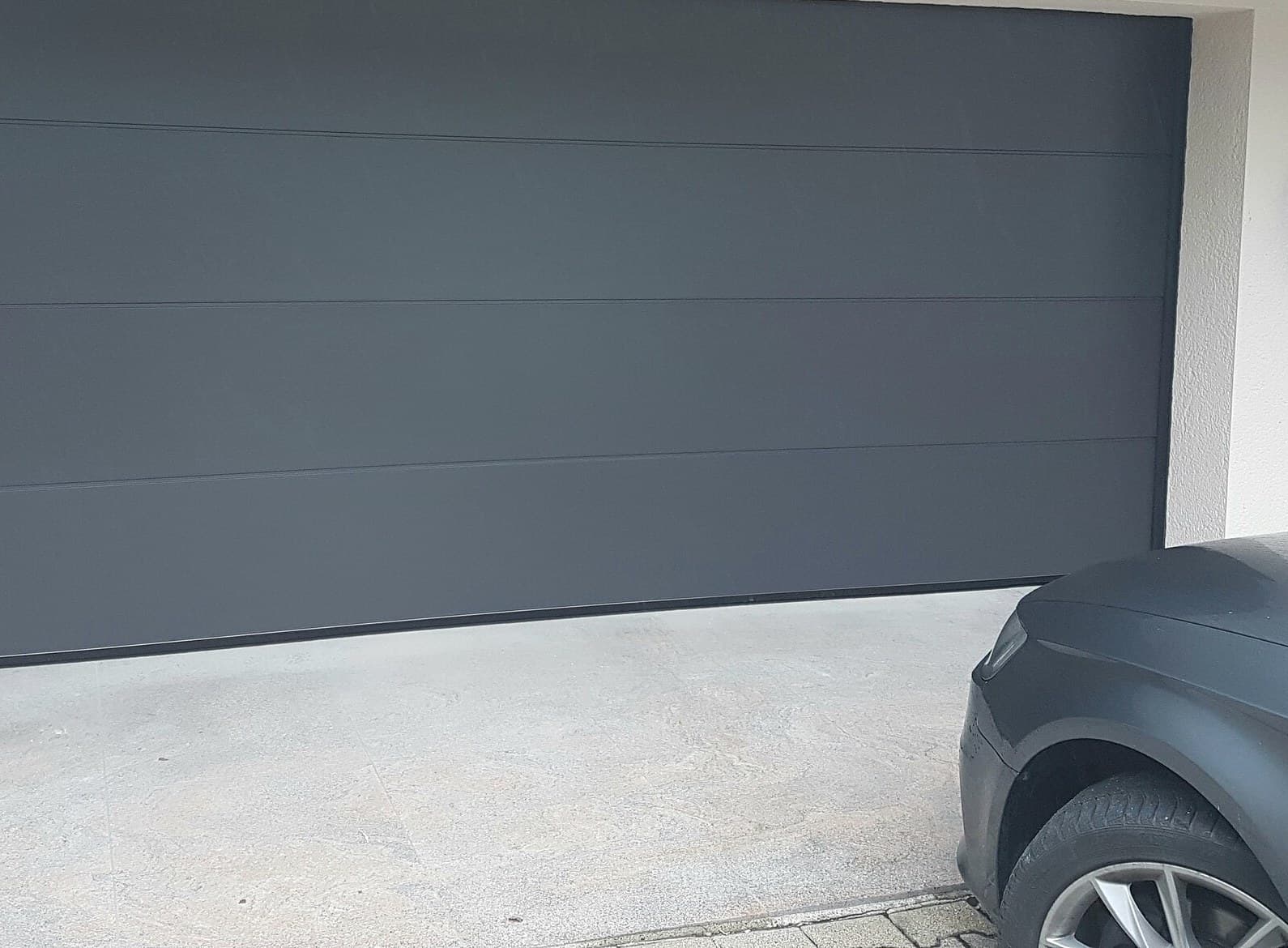 Porte de garage sectionnelle anthracite à panneaux lisses sur une façade enduite claire