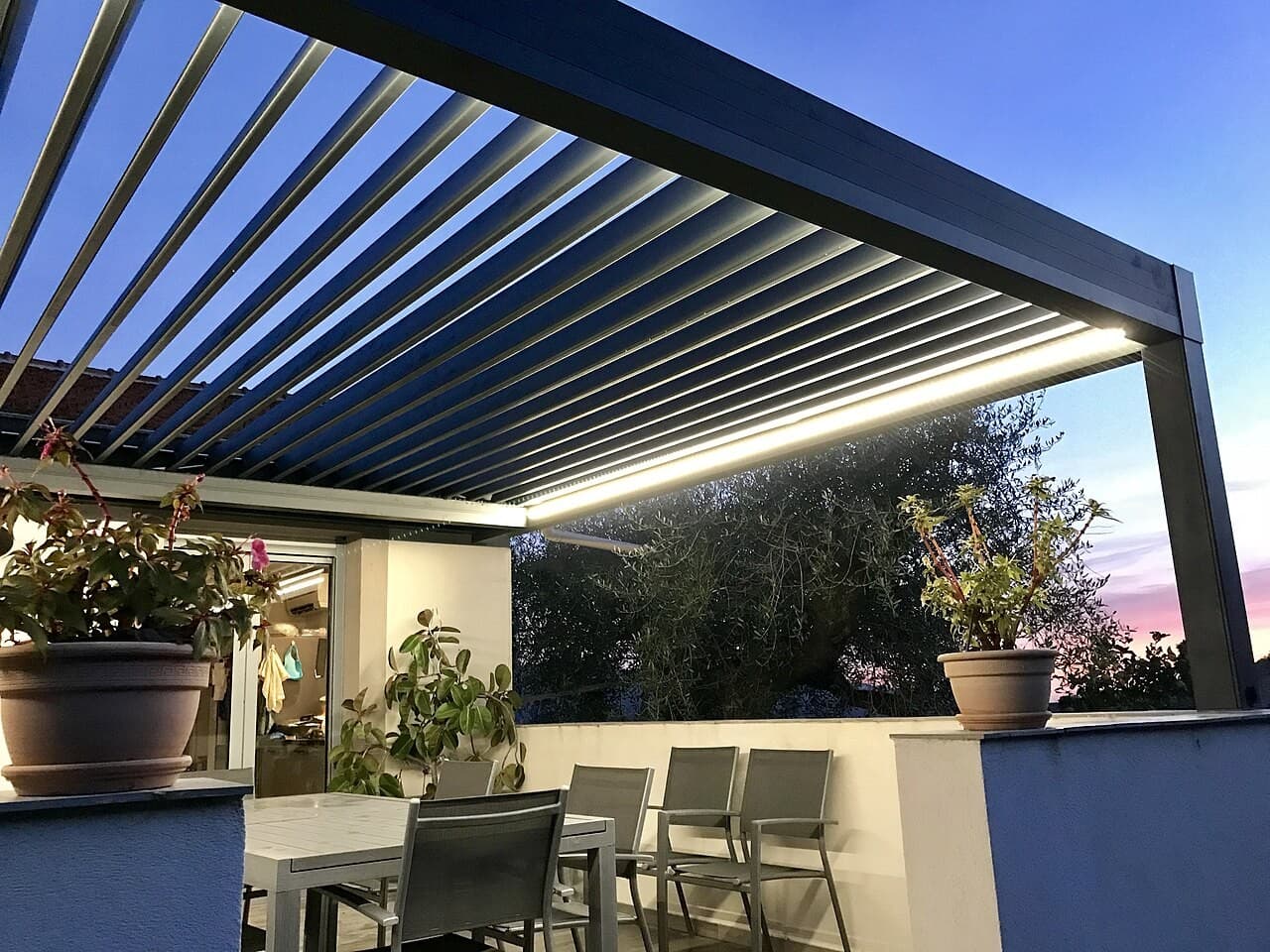 Pergola bioclimatique aluminium à lames orientables et éclairage LED sur une terrasse au crépuscule