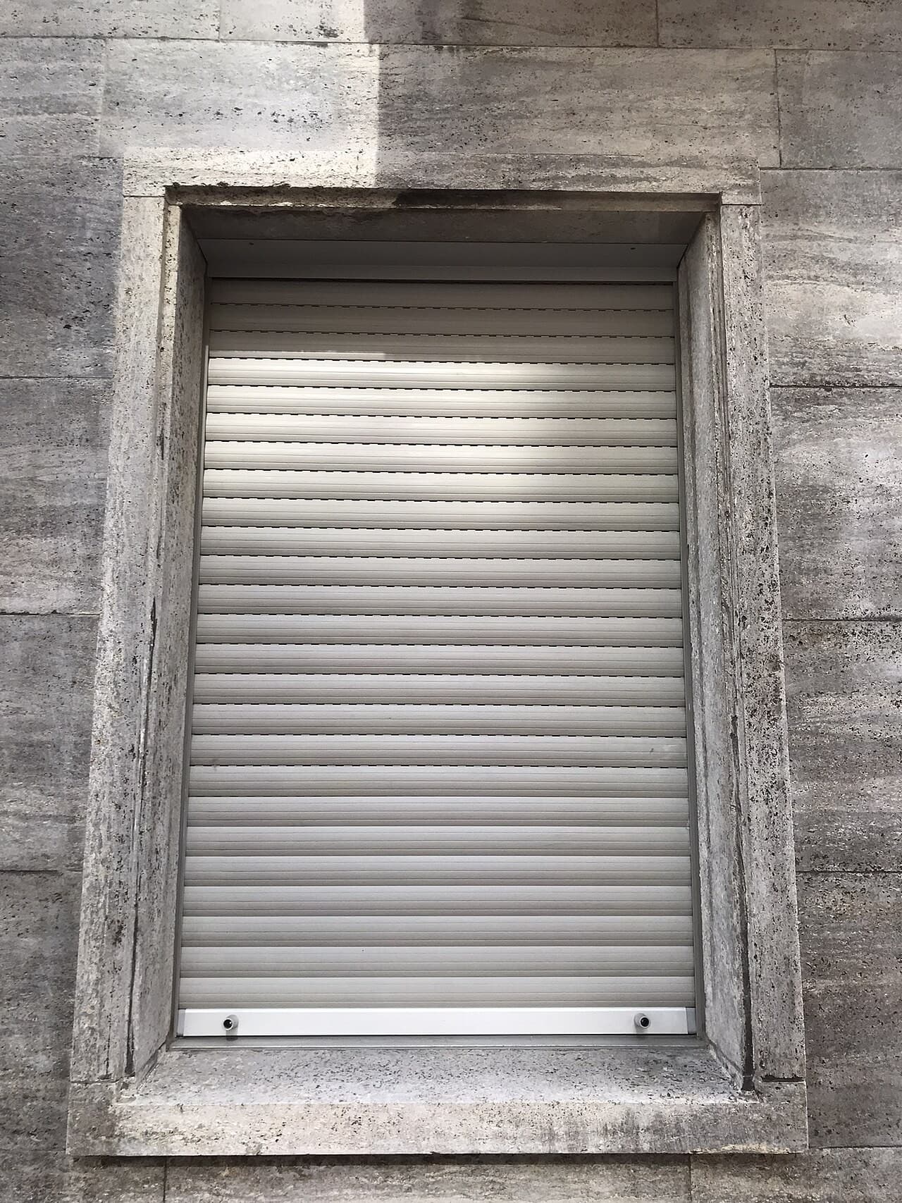 Volet roulant blanc en cours de fermeture sur une fenêtre à encadrement de pierre